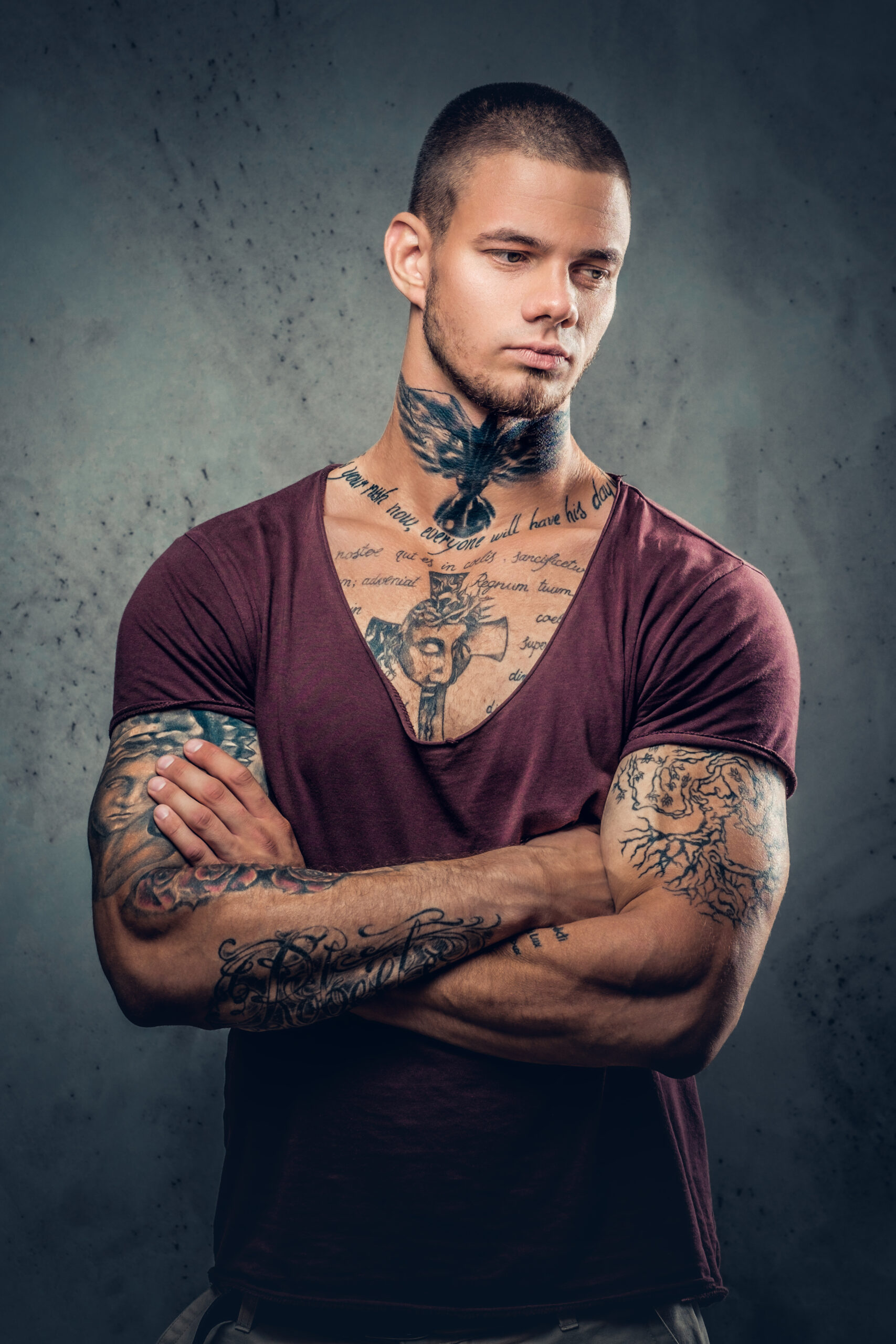 Tattooed male with crossed arms over grey artistic background.